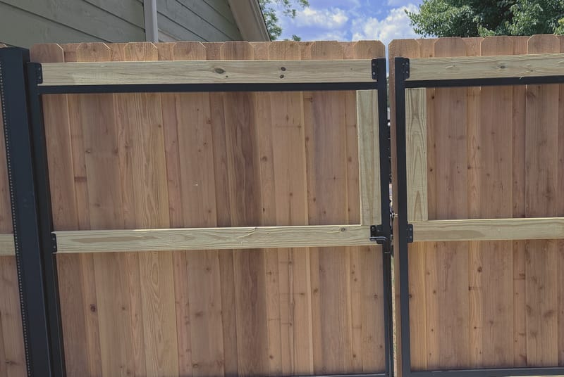 A double gate with black steel frames and black steel posts, filled with vertical boards and braced by pale horizontal rails, hung beside a matching fence.