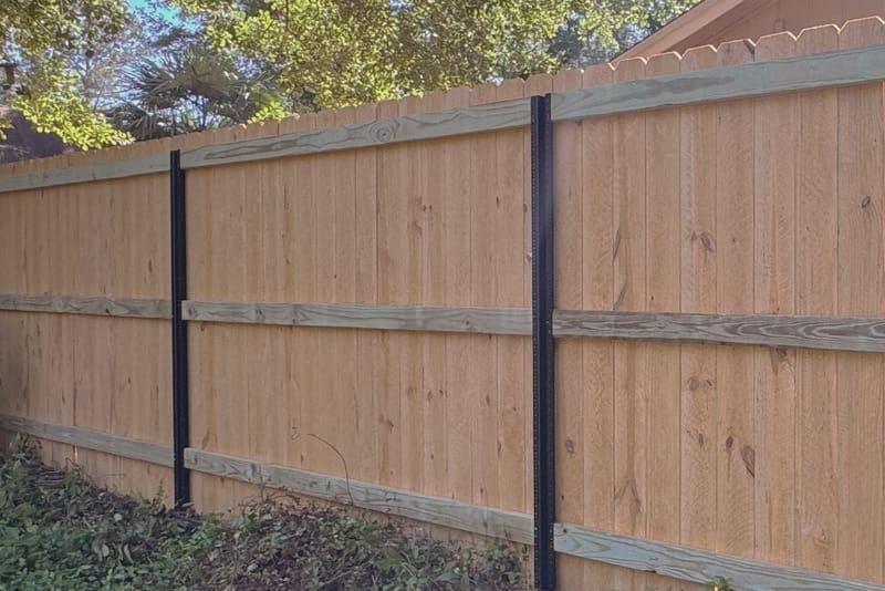 The back of a wood privacy fence, showing black steel posts with horizontal timber rails bolted across them behind the board faces.
